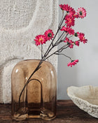 Vaas amber bruin glas H 20 cm met organische golvende vorm op een houten dressoir naast een crème kandelaar en een houten schaal voor een lichtgrijze muur