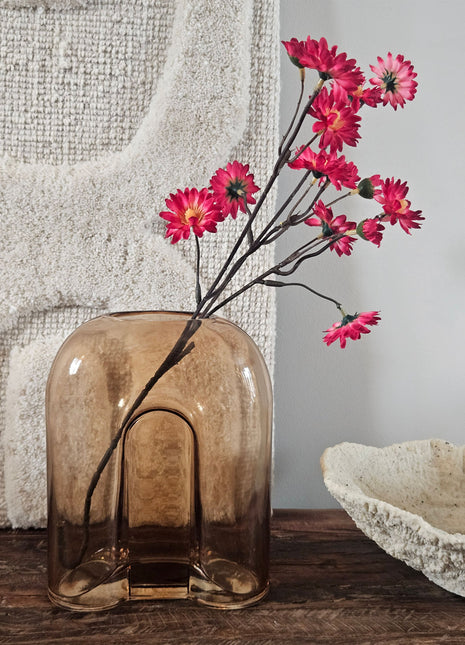Vaas amber bruin glas H 20 cm met organische golvende vorm op een houten dressoir naast een crème kandelaar en een houten schaal voor een lichtgrijze muur