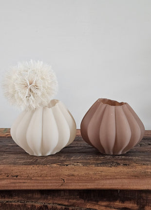 Vaas beige glas en vaas bruin glas Ø 14 x H 11 cm naast elkaar met een crème dandelion kunsttak op een houten ondergrond voor een lichtgrijze muur