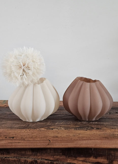 Vaas beige glas en vaas bruin glas Ø 14 x H 11 cm naast elkaar met een crème dandelion kunsttak op een houten ondergrond voor een lichtgrijze muur