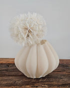 Vaas beige glas Ø 14 x H 11 cm met bolle ribbel-structuur en een crème dandelion kunsttak op een houten ondergrond voor een lichtgrijze muur