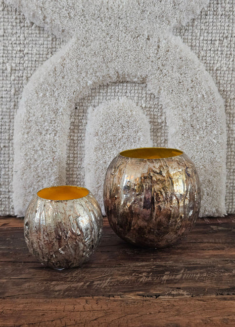 Bolvaas goud metaal S en M naast een hoge witte vaas met groene olijftakken voor een wit linnen wandpaneel met boogmotief op een houten dressoir