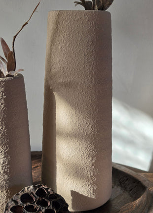 Close-up van beige Elora vaas met korrelige afwerking en bruine kunsttakken naast lotus op een houten dienblad