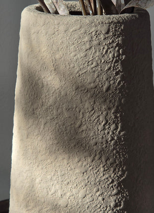 Close-up van beige Elora vaas met korrelige afwerking en bruine kunsttakken tegen een grijze achtergrond
