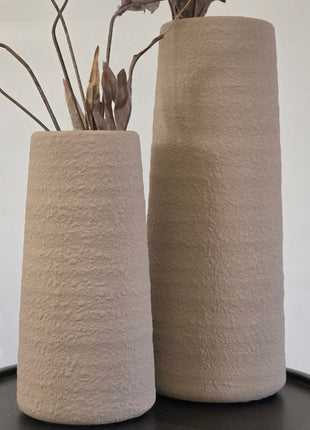 Vooraanzicht van twee beige Elora vazen met korrelige afwerking en bruine kunsttakken op een zwart tafeltje