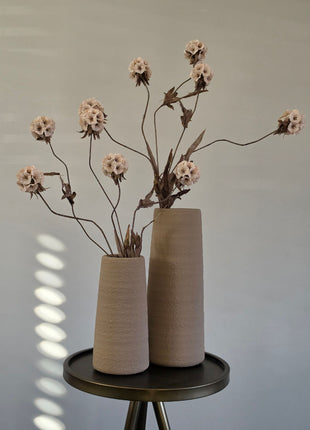 Vooraanzicht van twee beige Elora vazen met ruwe afwerking en beige kunstbloemen op een rond metalen tafeltje