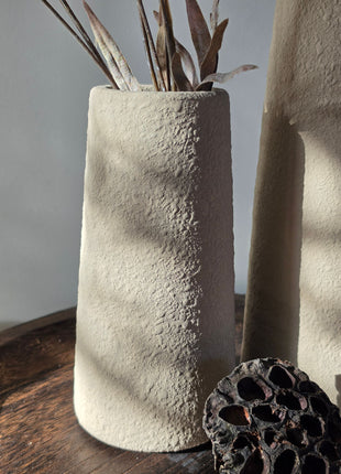 Close-up van beige Elora S vaas met korrelige afwerking en bruine kunsttakken naast lotus op een houten dienblad