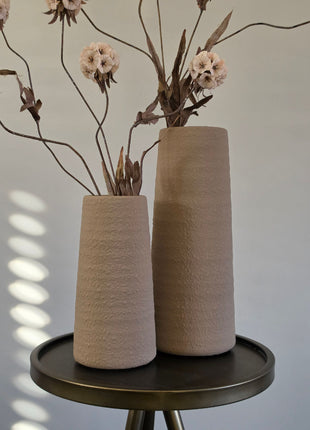 Vooraanzicht van twee beige Elora vazen met ruwe afwerking en creme kunstbloemen op een rond metalen tafeltje