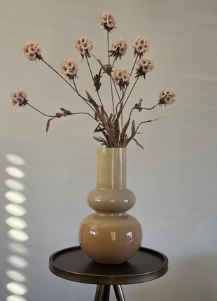 Vooraanzicht van taupe Livana vaas met glanzende afwerking en creme kunstbloemen op een rond zwart tafeltje