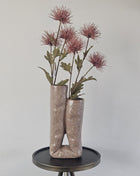Vaas Looped roze beige aardewerk met lus-vorm en matte afwerking hoogte 31 cm getoond op een bijzettafel. De vaas heeft kleurrijke bloemen.