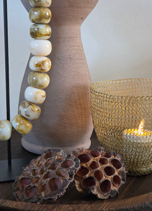 Close-up van taupe Marconne vaas met ruwe afwerking naast onyx kralen en goudkleurige lichthouder op hout