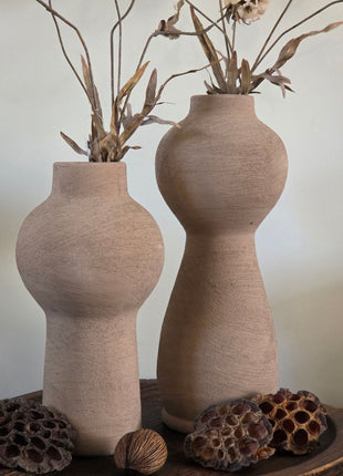 Vooraanzicht van twee taupe Marconne vazen met ruwe afwerking en beige kunstbloemen op een houten dienblad