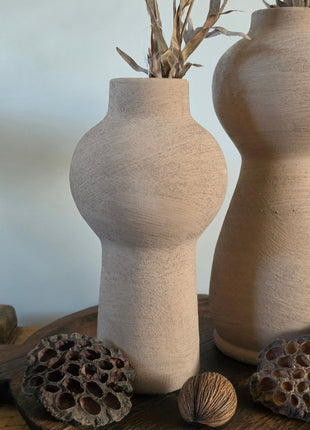 Vooraanzicht van taupe Marconne vaas met ruwe afwerking naast een grotere vaas en lotus op een houten dienblad