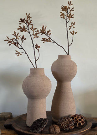 Vooraanzicht van twee taupe Marconne vazen met ruwe afwerking en bruine kunsttakken naast lotus op houten dienblad