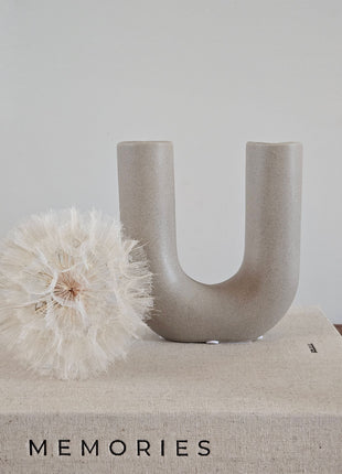 Vaas U vorm grijs aardewerk H 16 cm met brede U-opening en een roze zijdebloem op een houten ondergrond voor een lichtgrijze muur