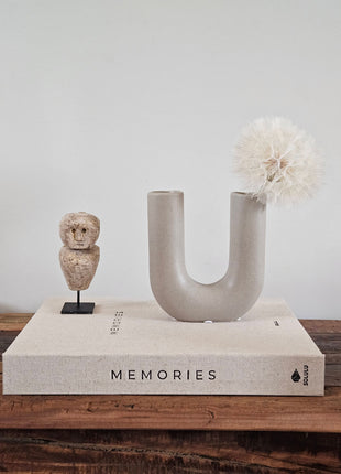 Vaas U vorm grijs aardewerk H 16 cm met brede U-opening en een crème dandelion kunsttak op een houten ondergrond voor een lichtgrijze muur
