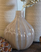 Vooraanzicht van taupe-bruine Velin vaas met glanzende ribbels en goudkleurige kunsttak naast lotus op hout