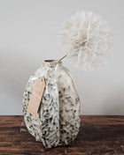 Vaasje Arquette beige-bruin keramiek M met platte ovale vorm en een crème dandelion kunsttak op een houten ondergrond voor een lichtgrijze muur