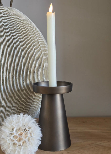 Kandelaar Viedma M van Vase the World in brons met een brandende LED dinerkaars op een donker houten oppervlak