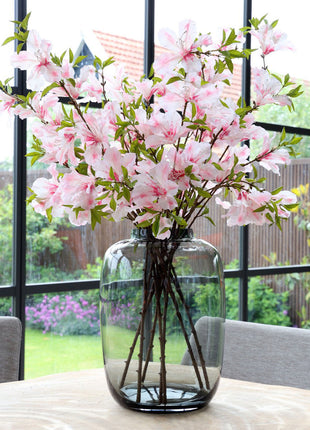 Vrijstaande vaas Artic M van Vase the World in glanzend taupe glas gestileerd met kleurijke bloemen op een tafel met op de achtergond een kleurrijke tuin.
