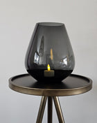 Vase the World vaas Tasman S grey Ø18 x H20 cm met druppelvorm en mondgeblazen glanzend grijs glas met een crème dandelion kunsttak op een houten ondergrond voor een lichtgrijze muur