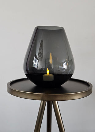 Vase the World vaas Tasman S grey Ø18 x H20 cm met druppelvorm en mondgeblazen glanzend grijs glas met een crème dandelion kunsttak op een houten ondergrond voor een lichtgrijze muur
