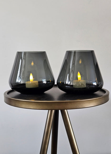 Vase the World waxinelichthouder Tasman in een prachtige grijze kleur. De waxinelichthouder is gemaakt van glas en is mondgeblazen. Afgebeeld als een set van twee op een sidetable.