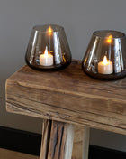 Vase the World waxinelichthouder Tasman in een prachtige Taupe kleur. De waxinelichthouder is gemaakt van glas en is mondgeblazen. Sfeerfoto van een set op een houten bijzet bankje