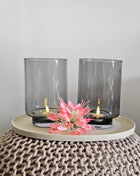 Set van twee Vase the World waxinelichthouders Thames XS grey in hoge conische vorm met brandende LED-kaars op een witte ondergrond