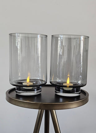Set van twee Vase the World waxinelichthouders Thames XS grey in hoge conische vorm met brandende LED-kaars op een witte ondergrond