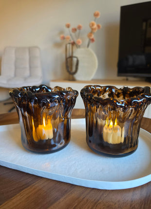 Twee waxinelichthouders Myron in donkerbruin glas naast elkaar op een houten ondergrond