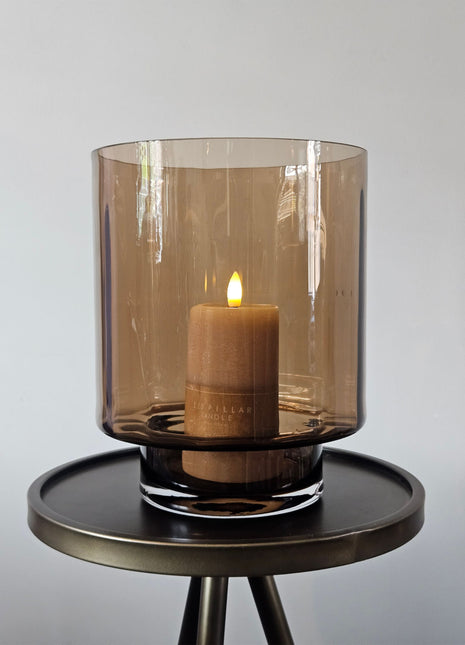 Cilindrisch windlicht Dune Taupe M in taupe glas met een dikke glazen bodem en een brandende LED-kaars op een houten ondergrond