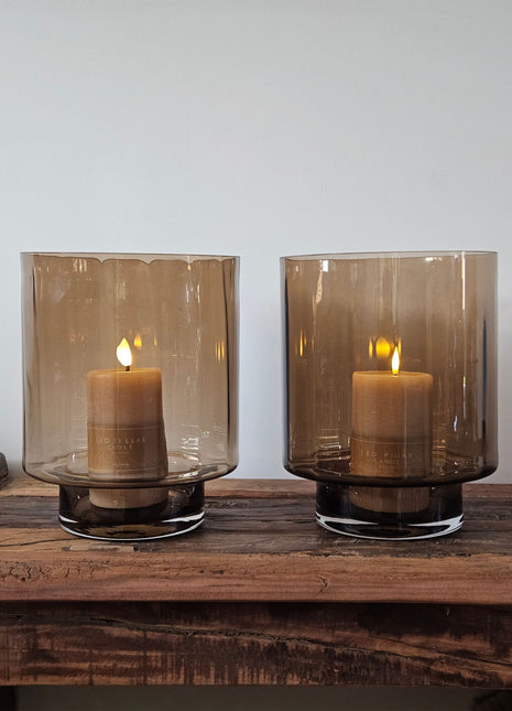 Twee cilindrische windlichten Dune Taupe in taupe glas met LED-kaarsen naast twee geribbelde aardewerk vazen met droogbloemen op een houten ondergrond