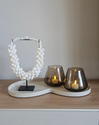 Woonaccessoire Set Ivory Lumi met een natuurlijk witte schelpenketting en twee taupe Tasman waxinelichthouders op een ivoor dienblad.