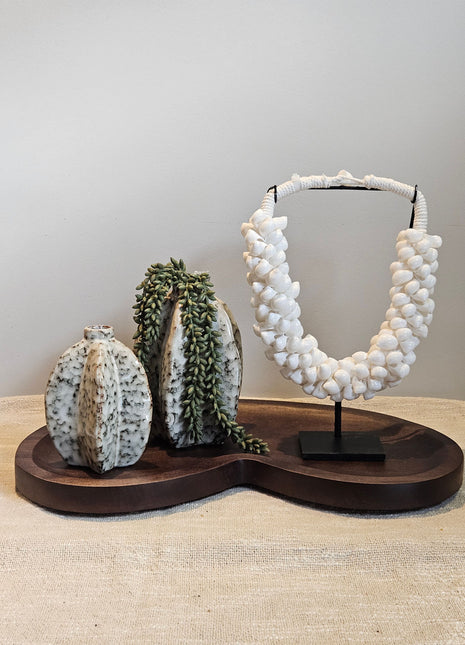 Decoratie Set Walnut Vase met twee keramieke Arquette vaasjes, een groene kunst erwtenplant en een witte schelpenketting op walnoot dienblad.