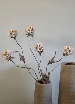 Vooraanzicht van creme Scabiosa zijdebloemen met stoffen bloemblaadjes in een beige vaas tegen een grijze muur